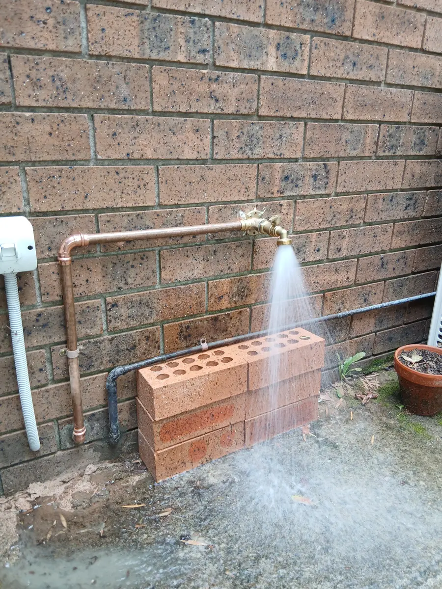 New copper outdoor water line being pressure-tested, water spraying out