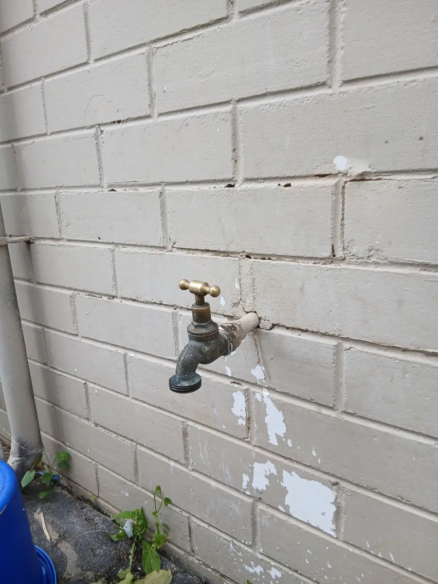 Worn brass garden tap on a painted brick wall before replacement