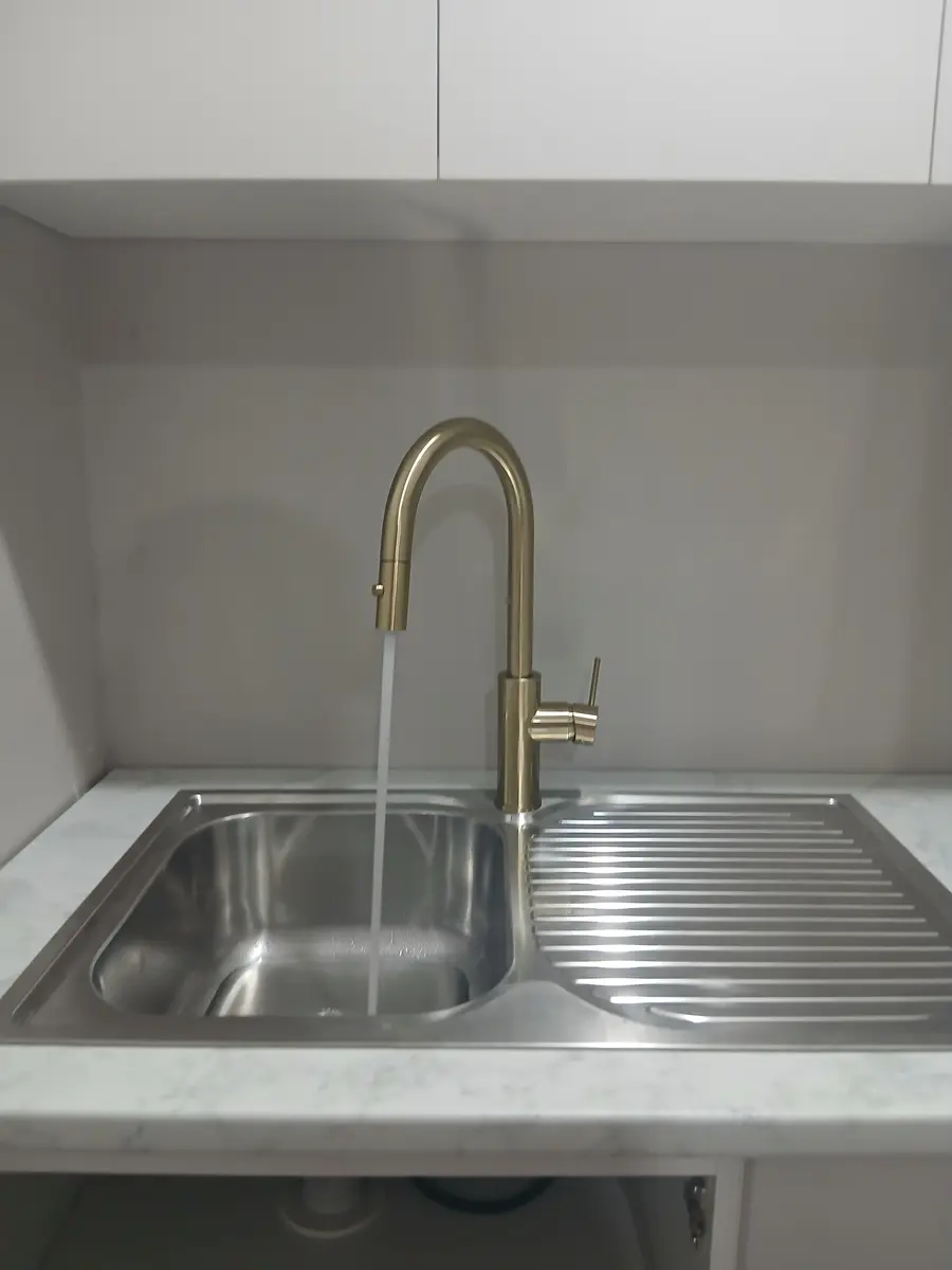 Brushed-gold pull-down kitchen mixer tap running over a stainless steel sink